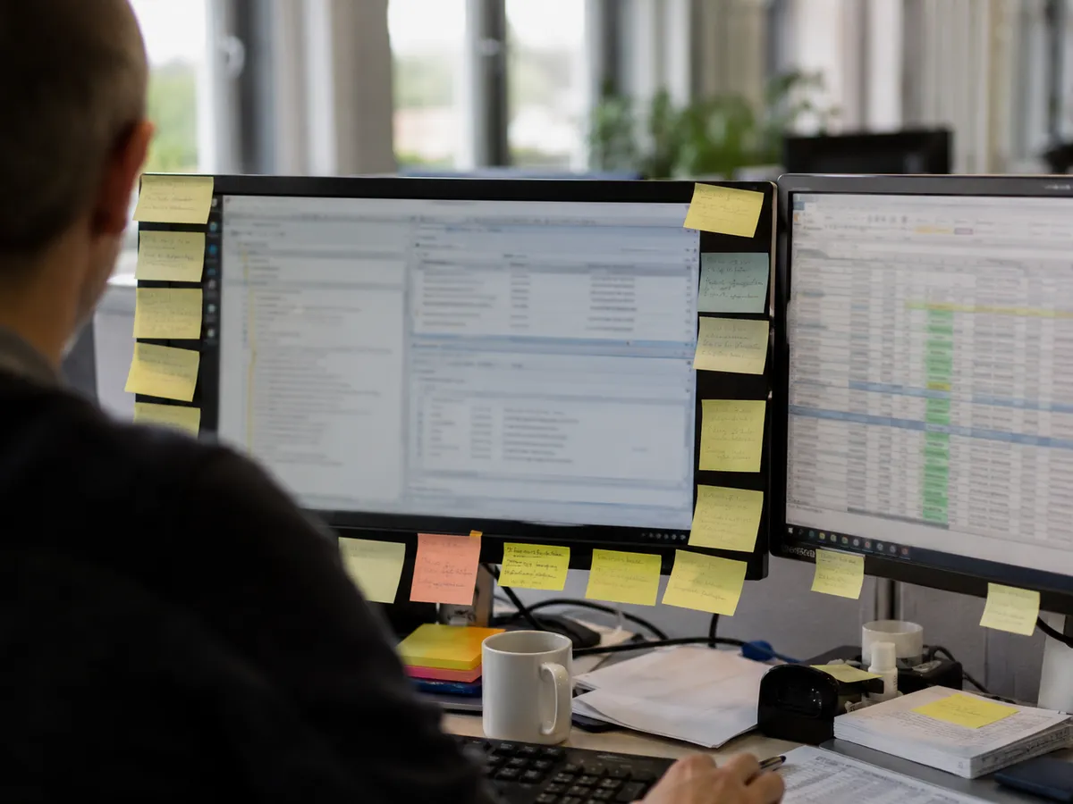 Bildschirm voller Haftnotizen und eine improvisierte Tabelle daneben - Arbeiten um die Software herum